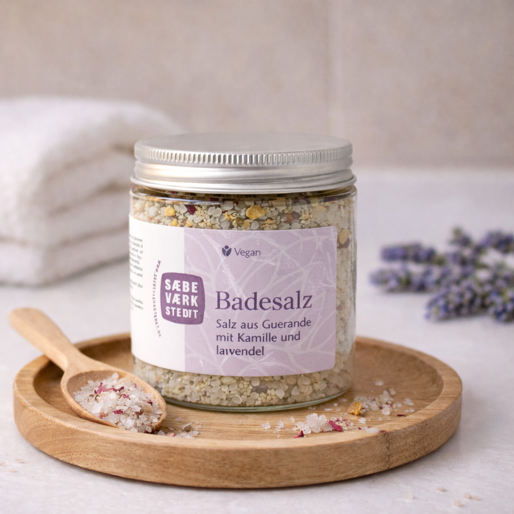 Ein offenes Glas Kamille & Lavendel Badesalz neben eHandtüchernund getrockneten Blüten auf einem Holztablett – symbolisiert Ruhe und Baderitual.
