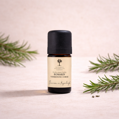 Flasche Bio ätherisches Öl Rosmarien auf beigeem, cleanem Studio-Hintergrund, mit Infusionszutaten passend zum Öl im Hintergrund. 100 % naturrein, biologisch, pflanzlich und vegan, aus biodynamischem Anbau und Handernte, transparent hergestellt von Pflanze bis Abfüllung.