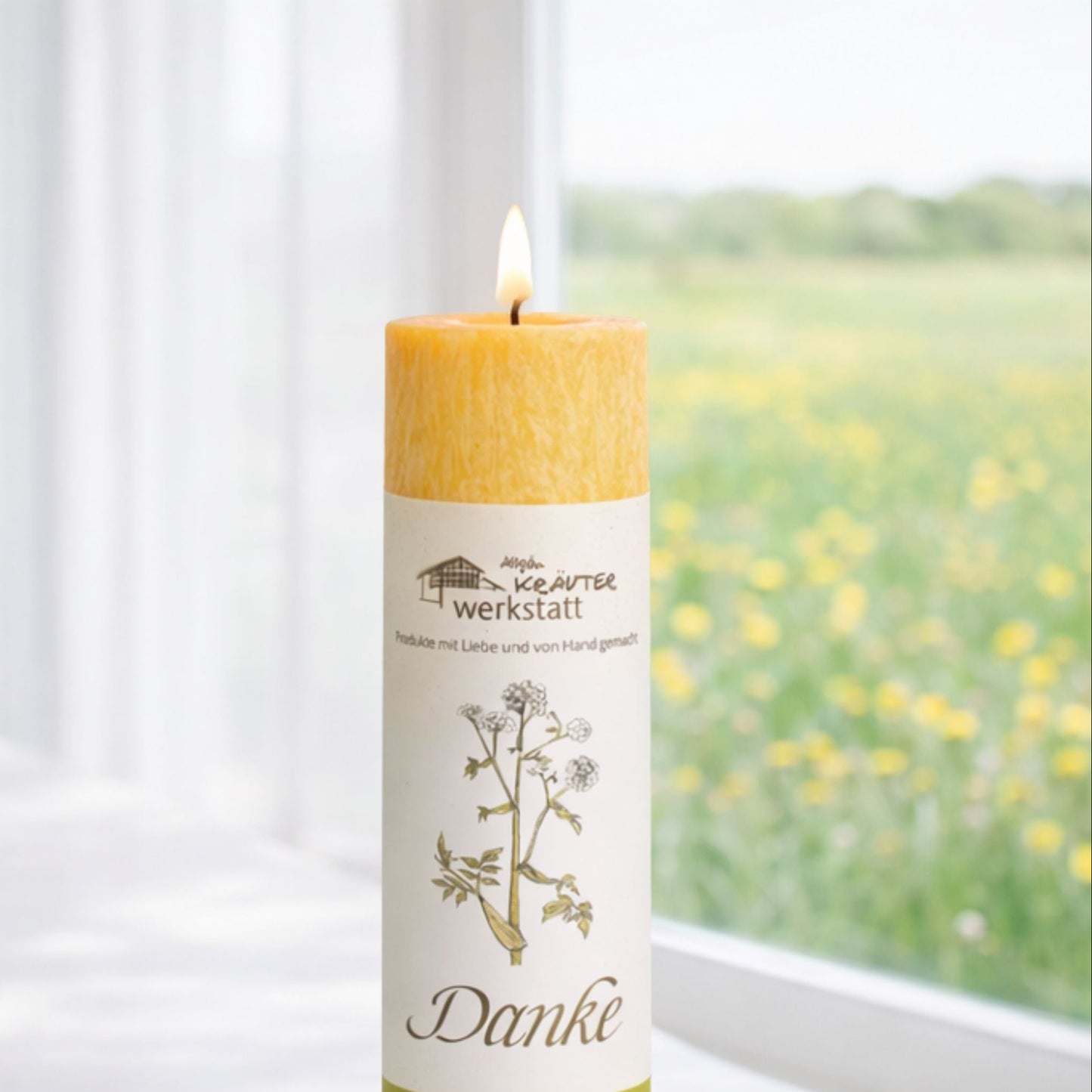 Heilkräuterkerze Danke aus dem Allgäu an Fenster in Close up Baumwolldocht-Flamme und Label.