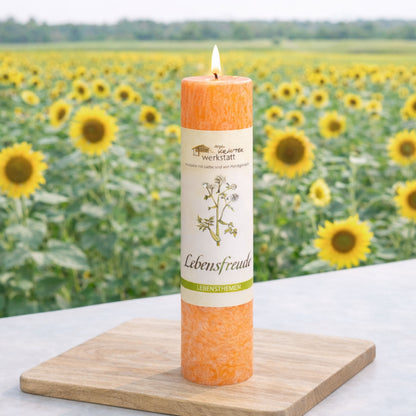 Heilkräuterkerze Lebensfreude vor Sonnenblumenfeld. Natürliche vegane Kerze die Freude spendet.